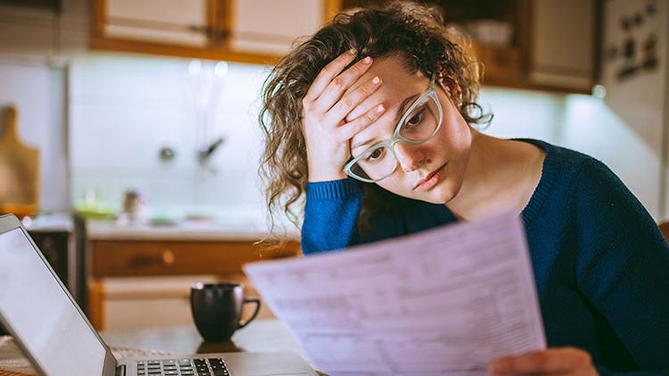 Woman at home reading paperwork at kitchen table trying to figure out how to pay her rent